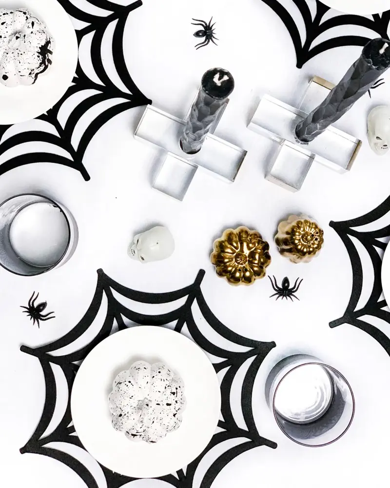 Black spider web placemats under white plates with black candles and gold pumpkins