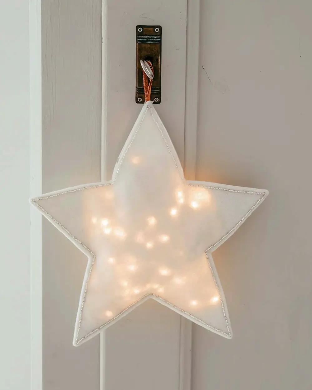 White star-shaped lantern with fairy lights inside hanging from a door hook