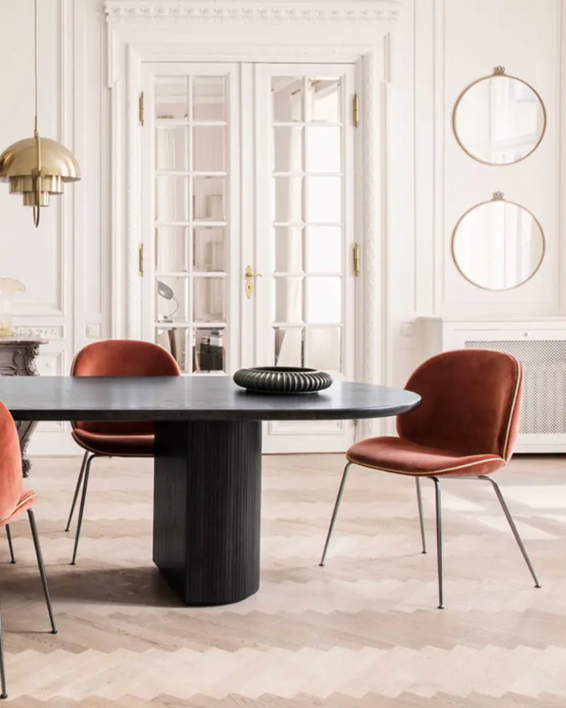 White dining room with a black oval table and rust velvet chairs