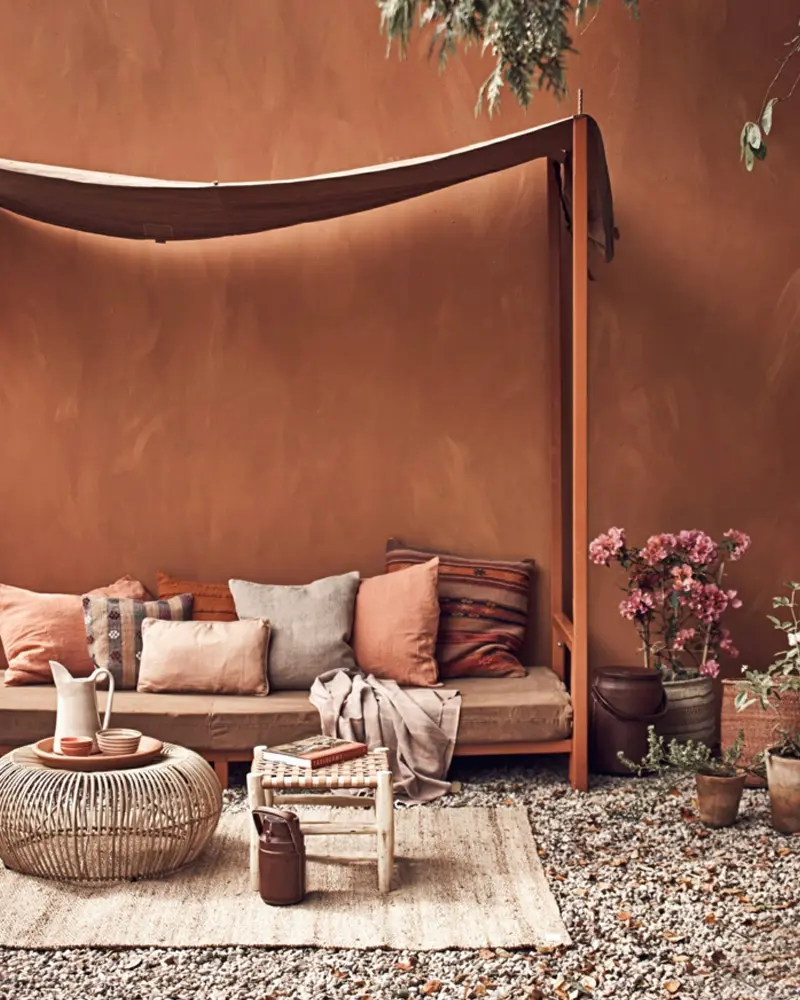 Earthy terracotta lounge corner with a daybed, cushions, rattan table and plants