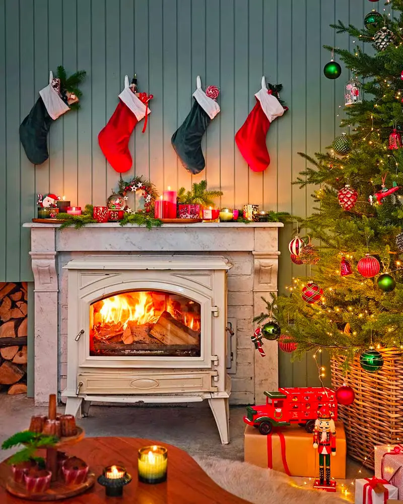 Red and green stockings above a white wood stove, a tree with red ornaments and a nutcracker