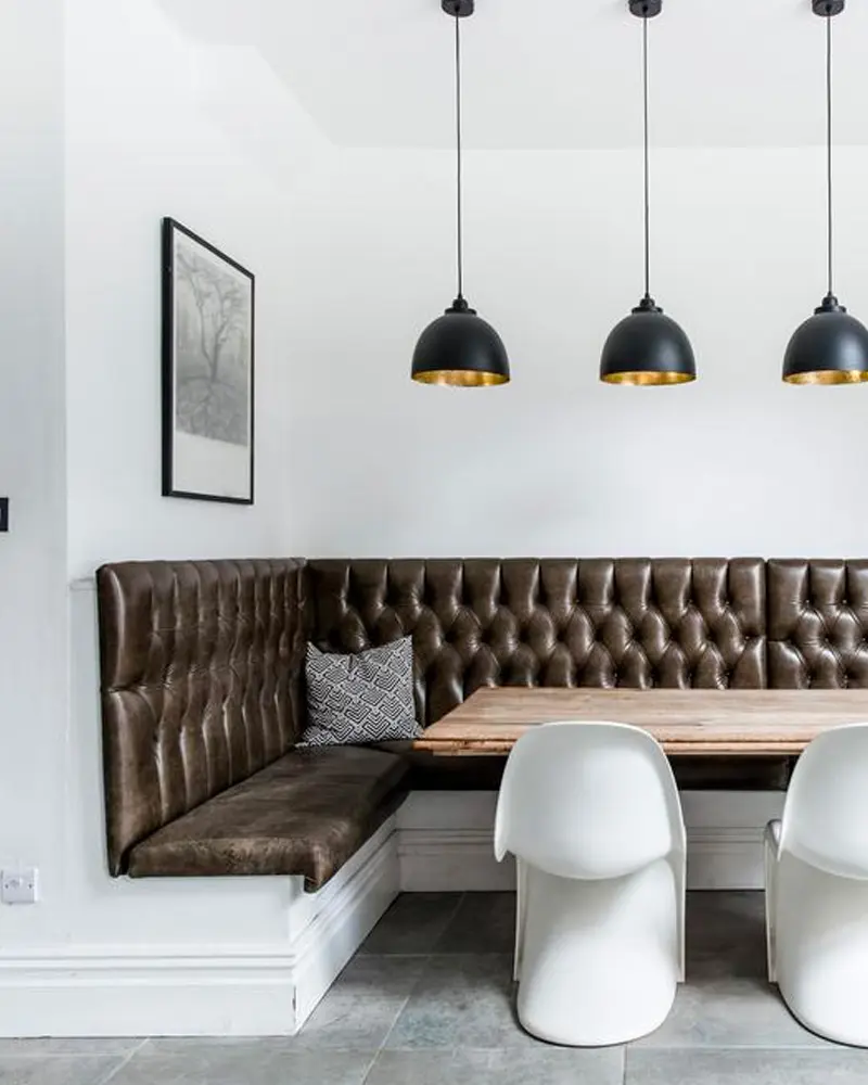 Brown tufted leather corner banquette with white chairs and black pendant lights