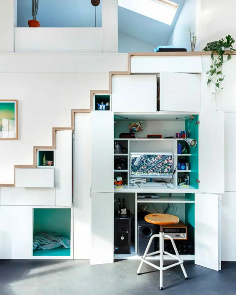 White under-stairs storage with a teal-lined computer nook and wood stool