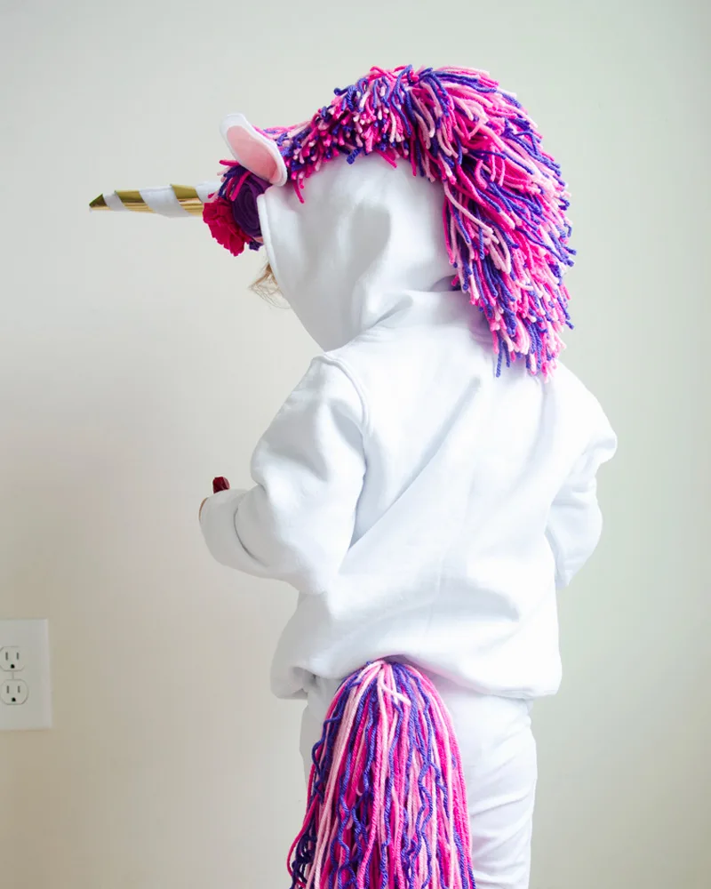 White hoodie with a pink and purple yarn mane, gold horn and yarn tail seen from behind