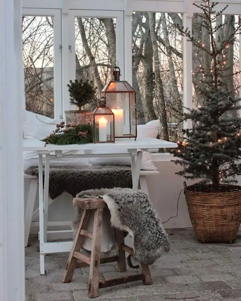 Sunroom with a small tree in a wicker basket, lanterns and sheepskin on a wooden stool