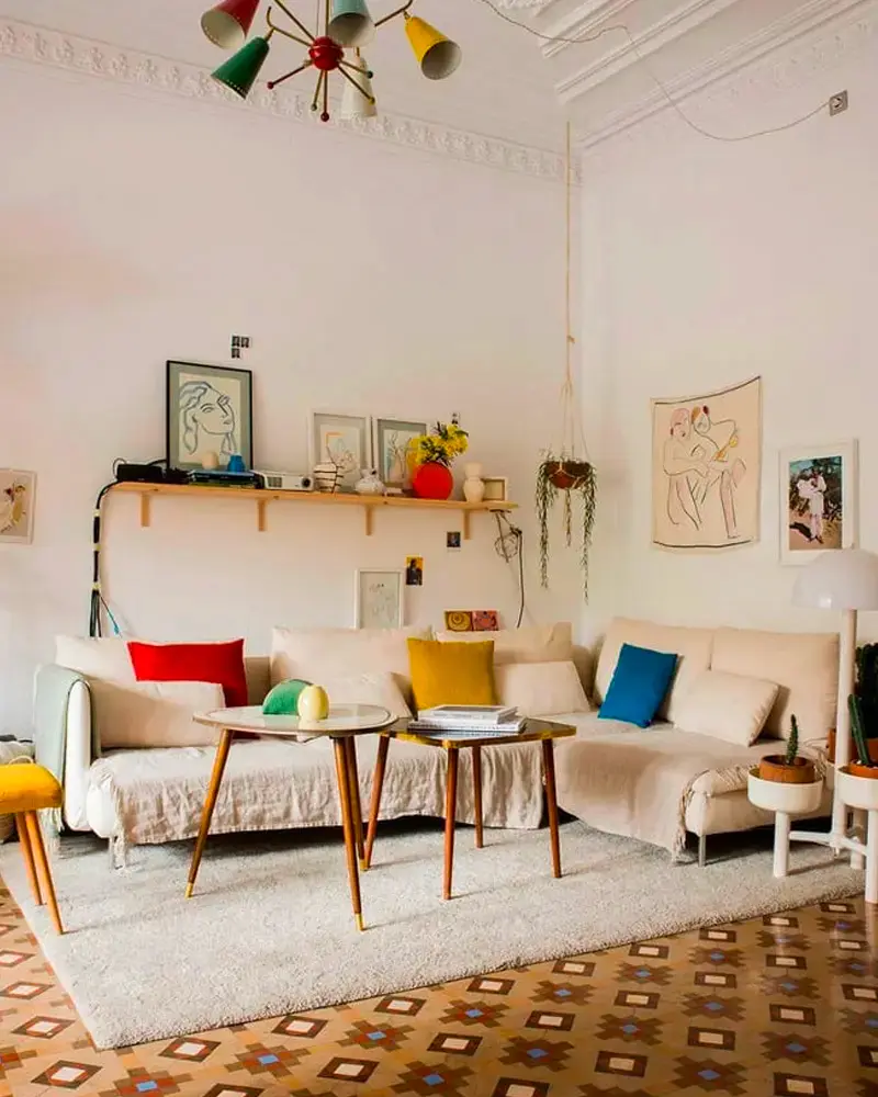 Vintage living room with cream sofas, red, blue and yellow pillows, wood tables, a patterned rug and a colorful Sputnik chandelier
