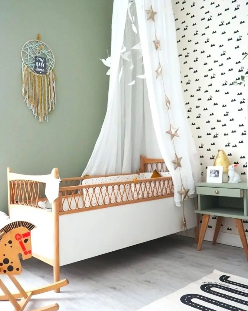 Sage green nursery with white cane crib, star canopy and black and white patterned wallpaper