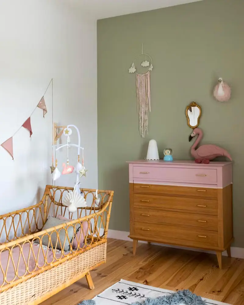 Nursery with olive green wall, rattan crib, pink-topped dresser and plush flamingo