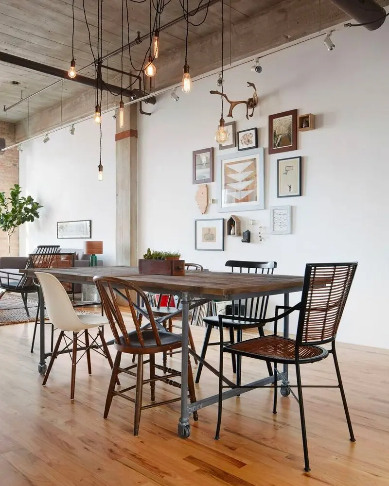 Wood table on metal casters with mismatched chairs, bare Edison bulbs and a gallery wall