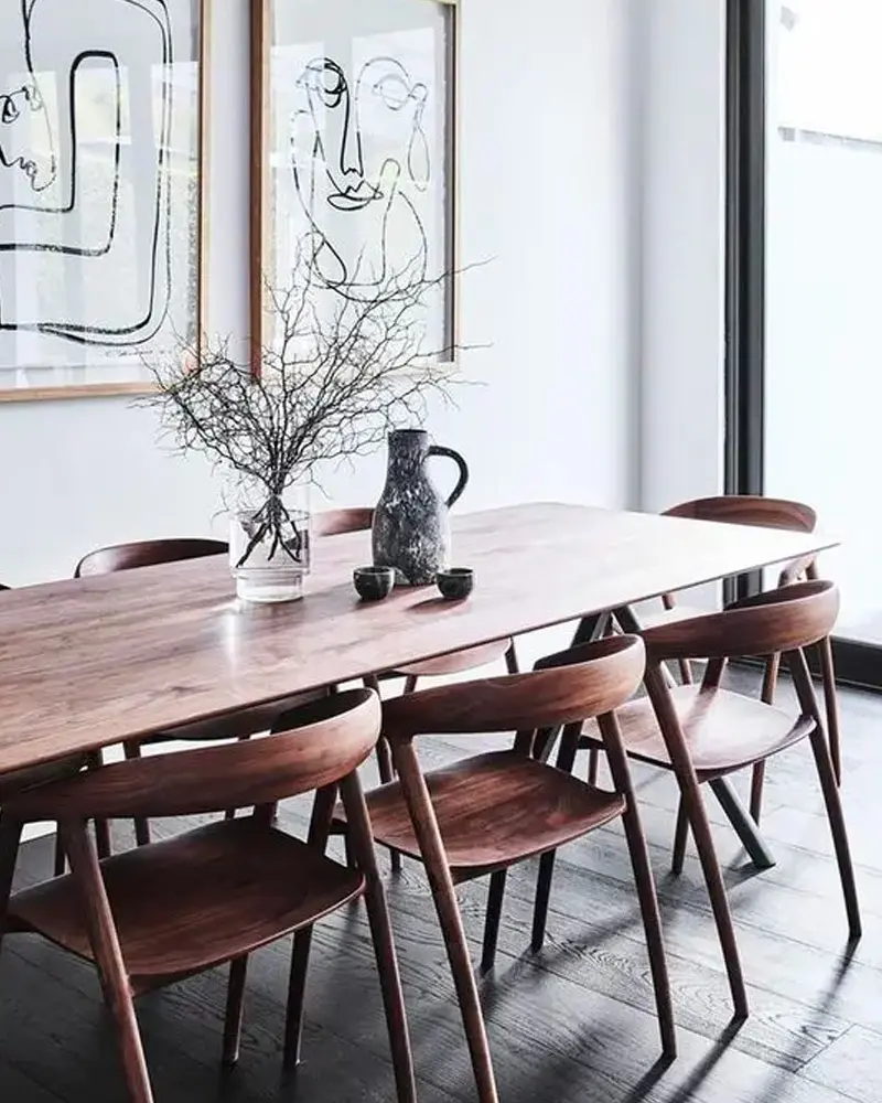 Walnut dining table and curved-back chairs with bare branches in a vase and line-drawing art