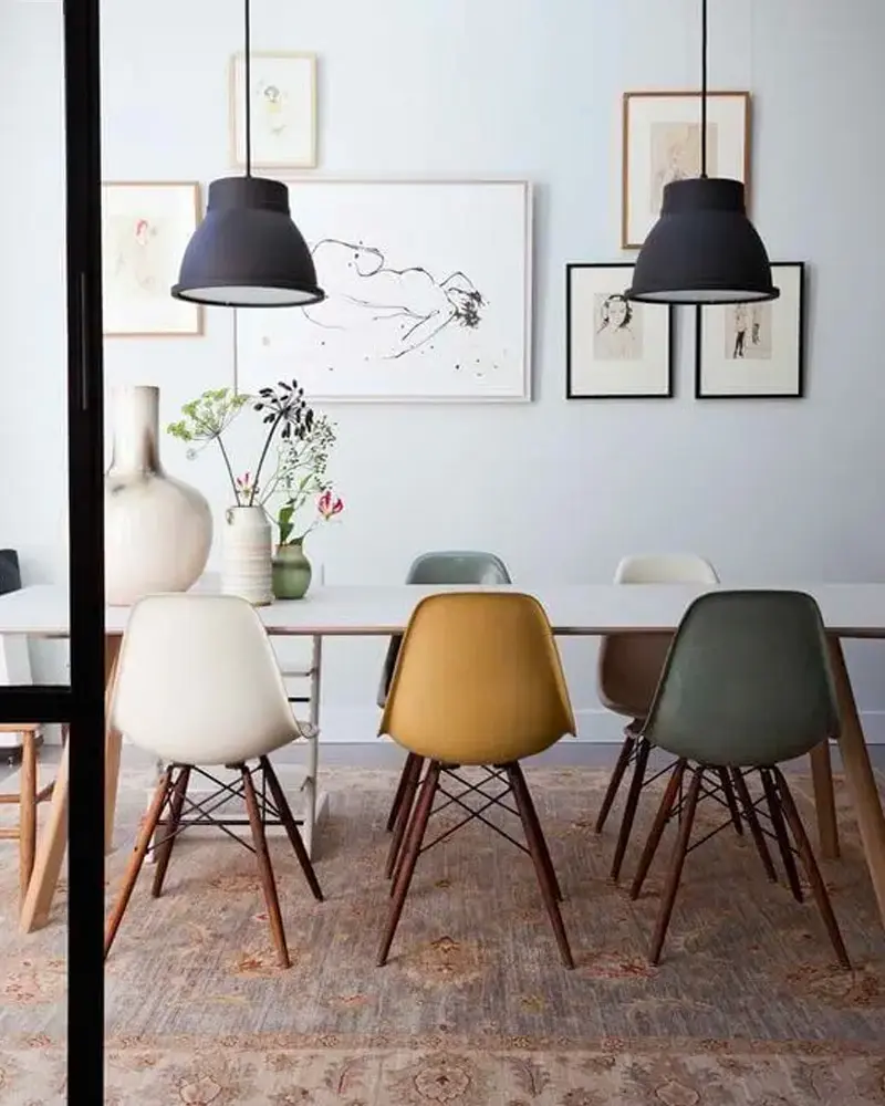 Dining table with mismatched molded chairs in mustard, sage and white under black pendant lights