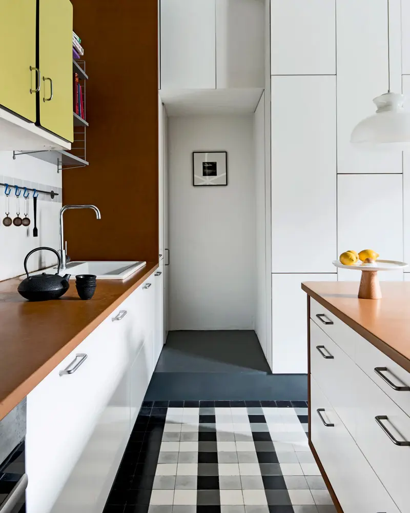 Galley kitchen with wood counters, white cabinets and black and white checked rug