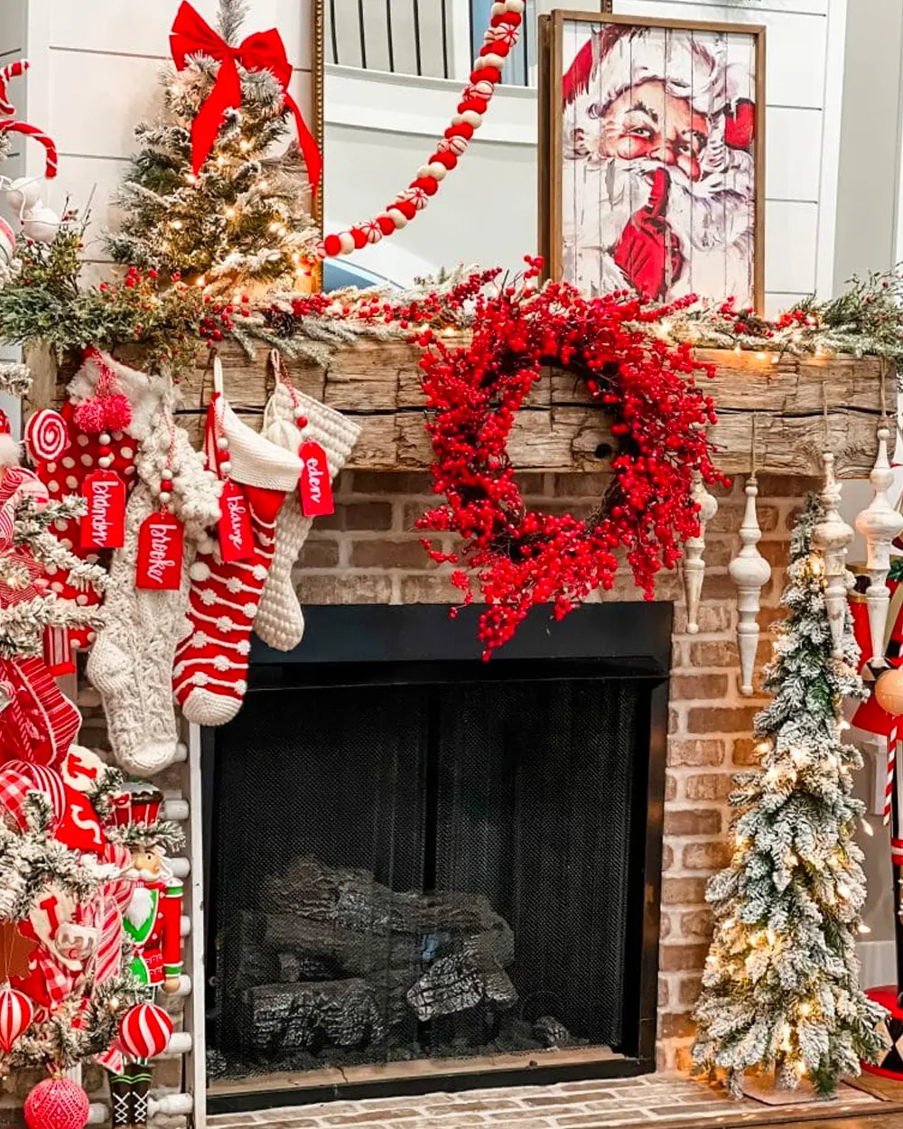 Brick fireplace with a red berry wreath, candy cane stockings, a vintage Santa print and mini trees