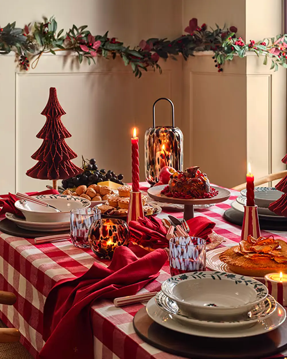 Christmas table with red gingham tablecloth, red paper tree, red taper candles and a garland