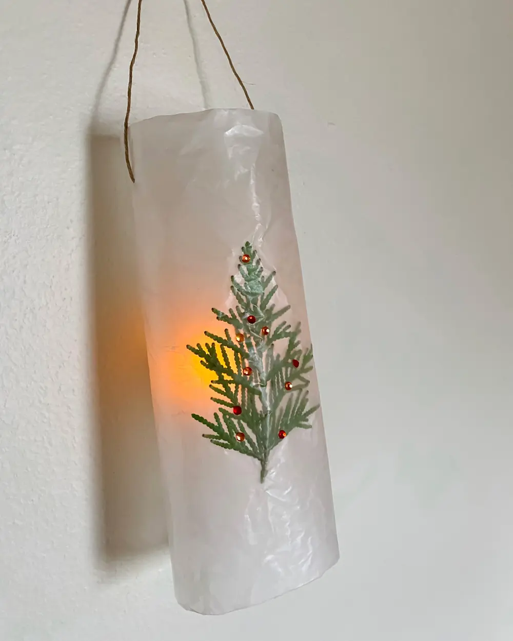 Wax paper hanging lantern with a pressed fir sprig and red dots glowing from inside