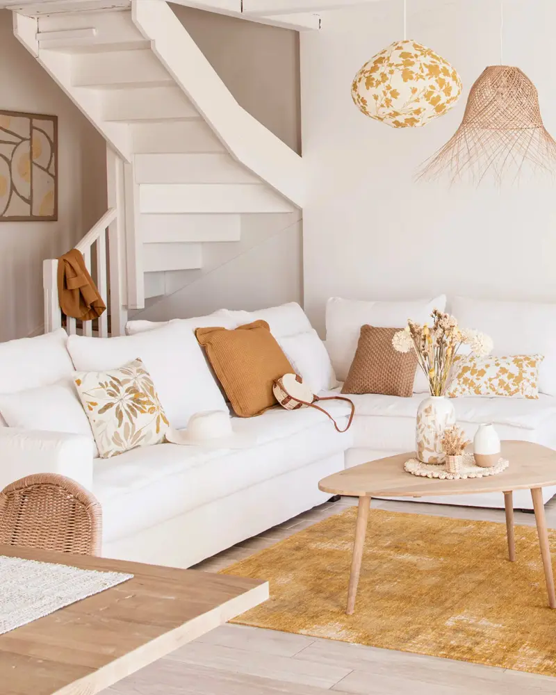 White sofa with mustard and ochre pillows, round wood coffee table, honey rug and floral pendant