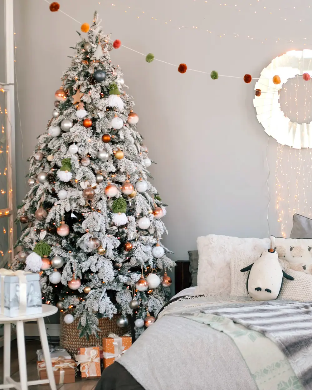 Bedroom with a flocked tree with copper ornaments, a felt pom-pom garland, white bedding and a round mirror