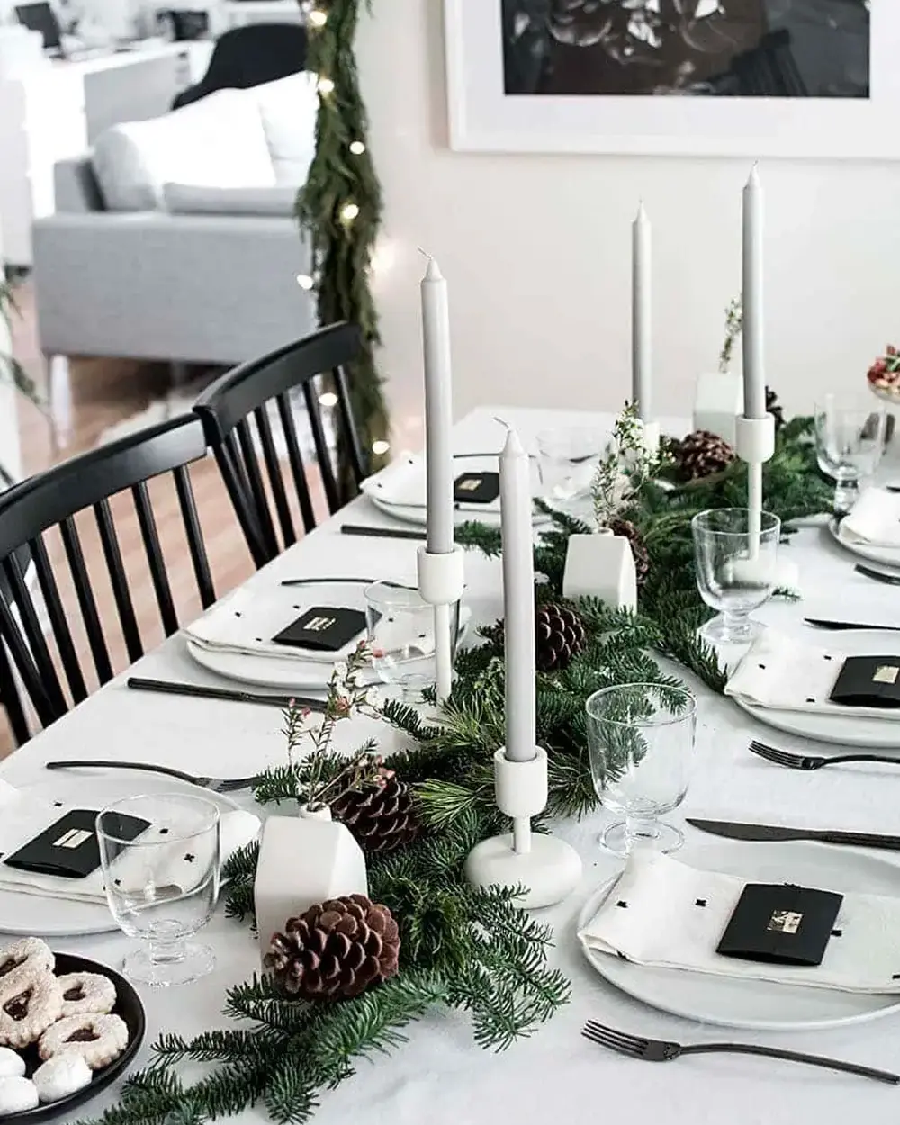 Black and white Christmas table with black napkins, tall white candles, pinecones and a fir garland down the center