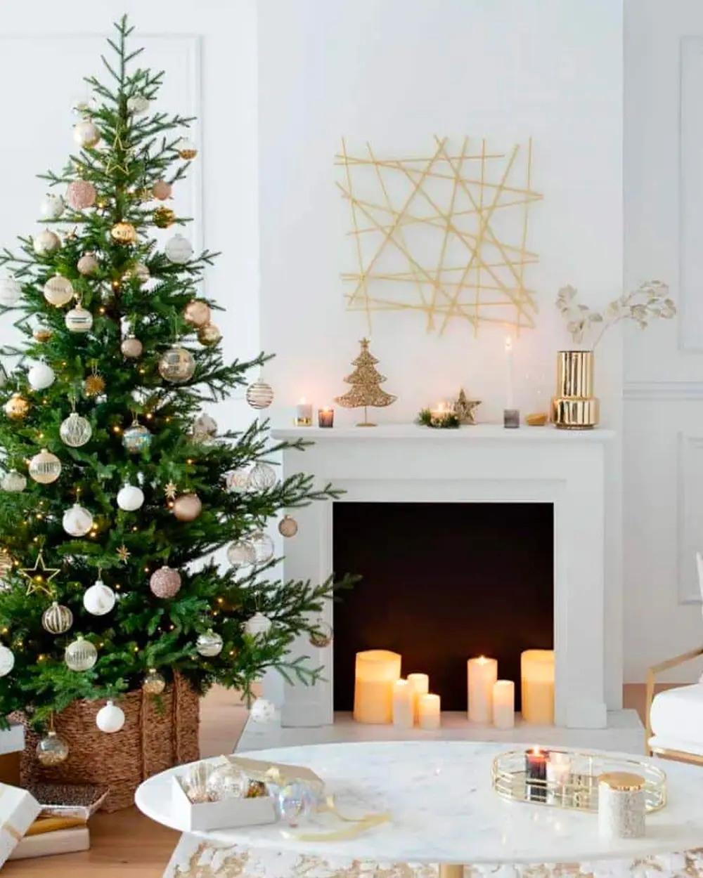 Green tree with white and gold baubles beside a white fireplace filled with pillar candles and gold accents