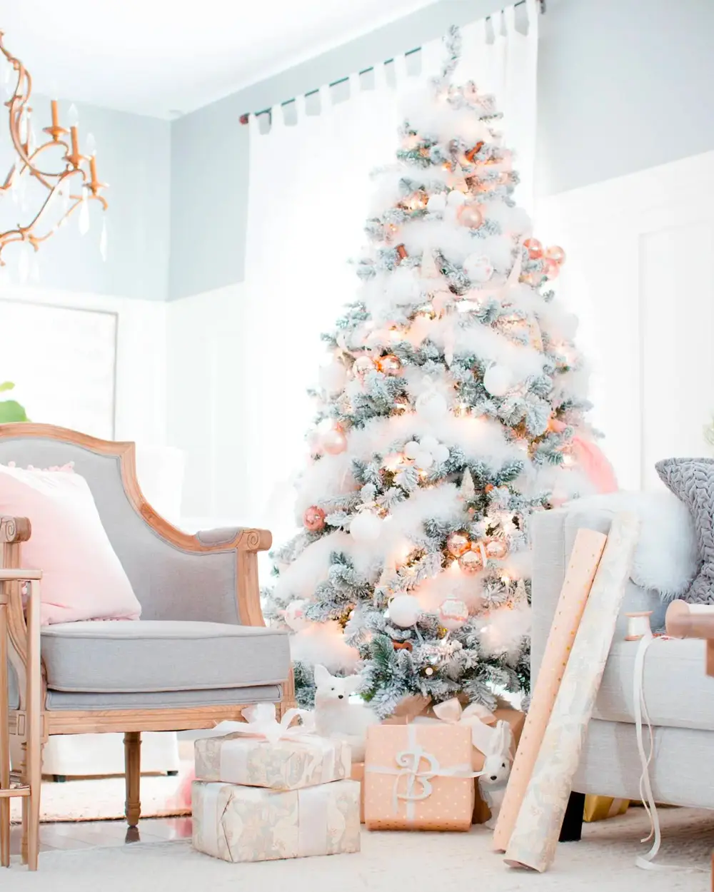 Heavily flocked white tree with blush ornaments, gray armchair with pink pillow and wrapped gifts