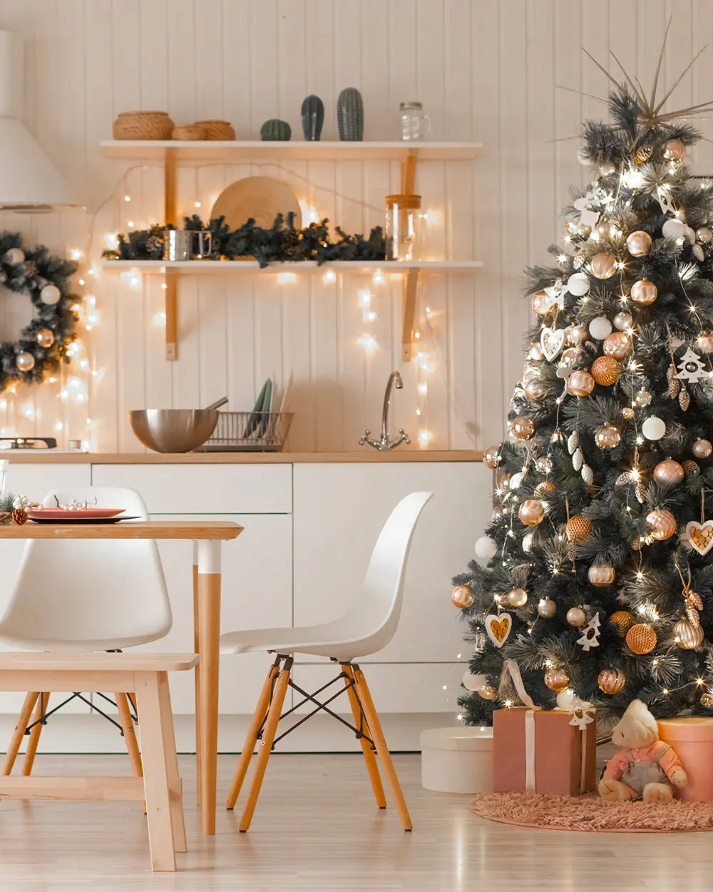 White kitchen with a light wood table and shelves, string lights, a wreath and a tree with copper baubles