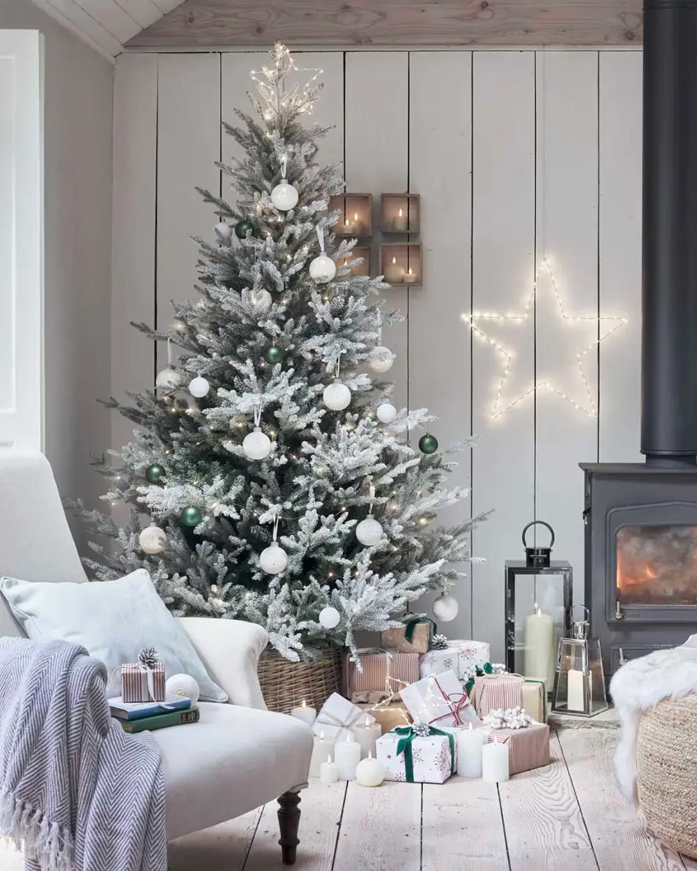 White-painted plank walls, a frosted tree with white baubles, a black wood stove, lanterns and a lit star