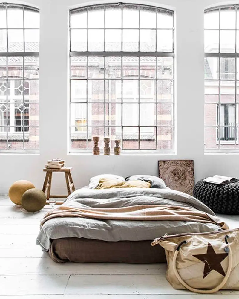 Low bed under large arched factory windows