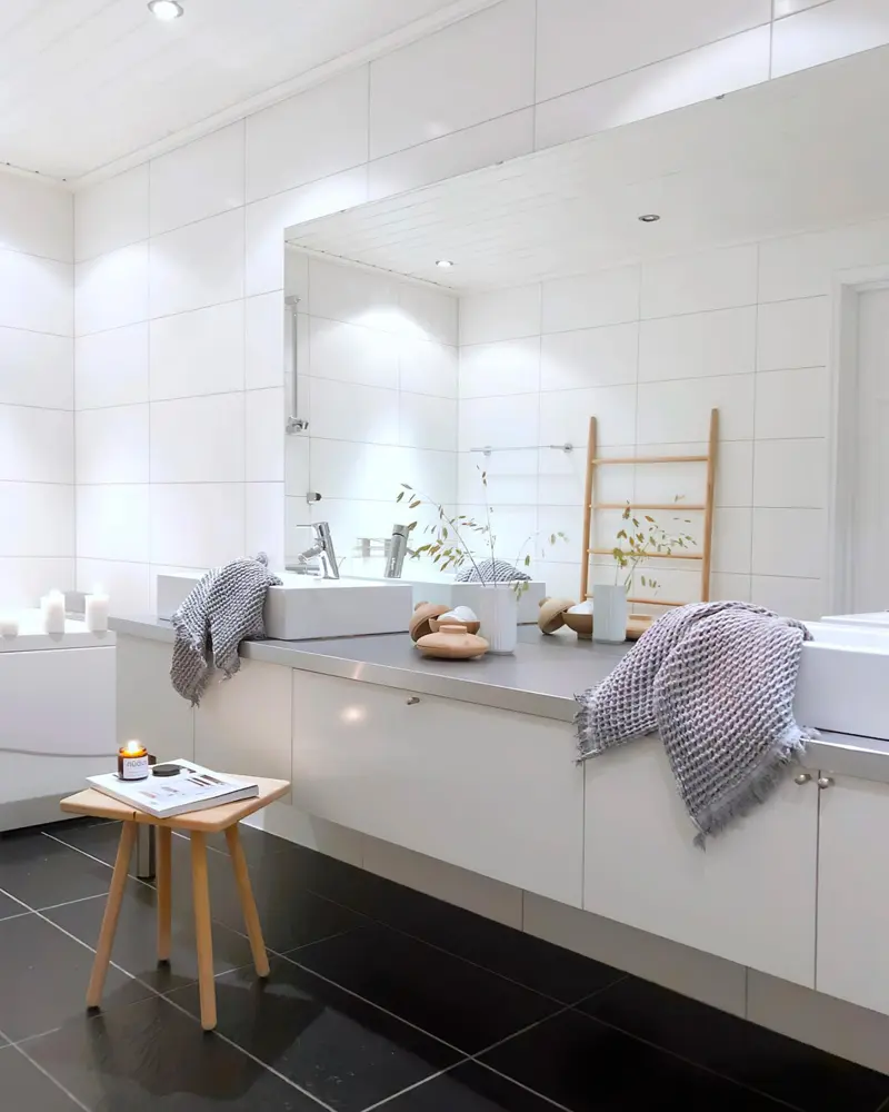 Large white bathroom with long mirror, floating white vanity, knit towels and wood stool