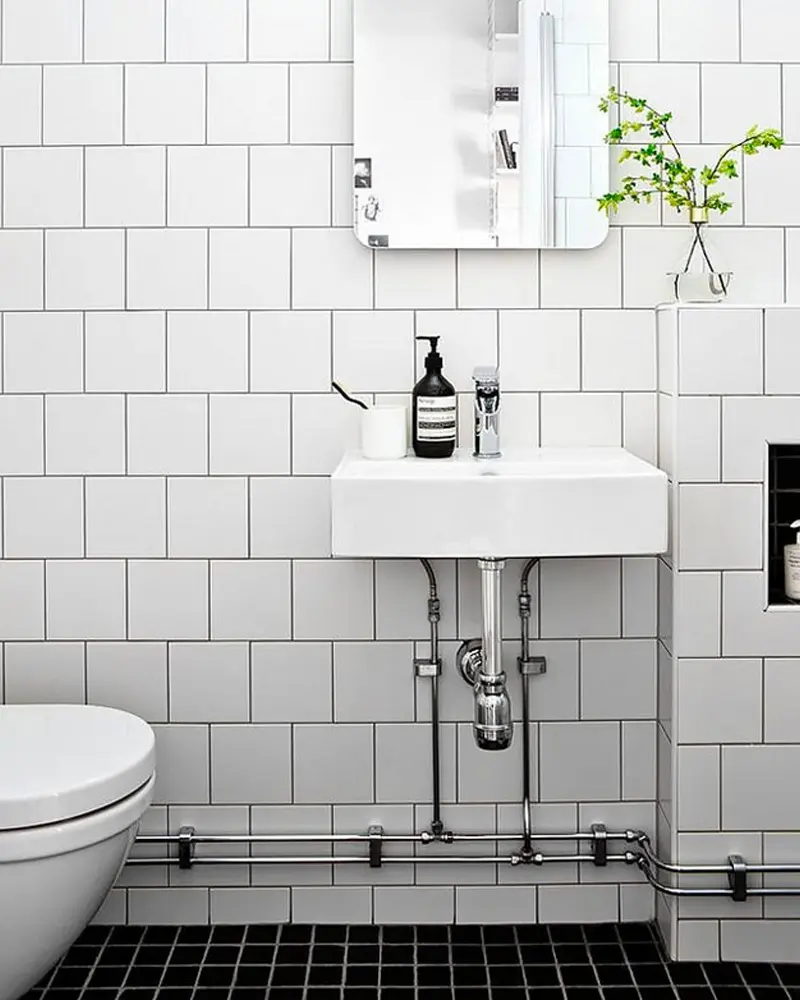 White square wall tiles, wall-mounted sink with exposed pipes and black floor tiles