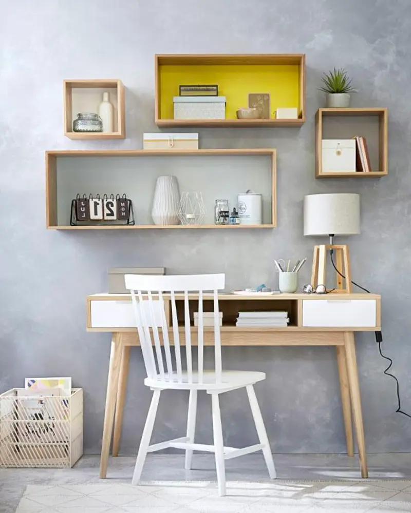 Wood and white desk with spindle chair under a wall of wood display boxes, one painted yellow