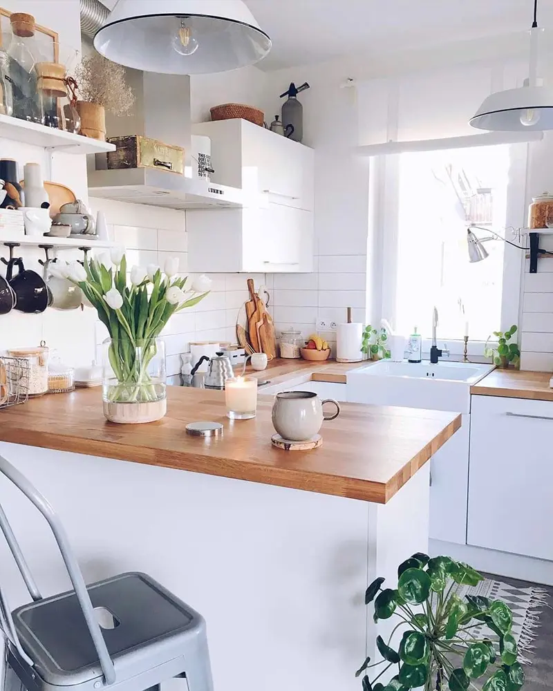 White kitchen with butcher-block counter, open shelves, enamel pendant lights and tulips in a vase