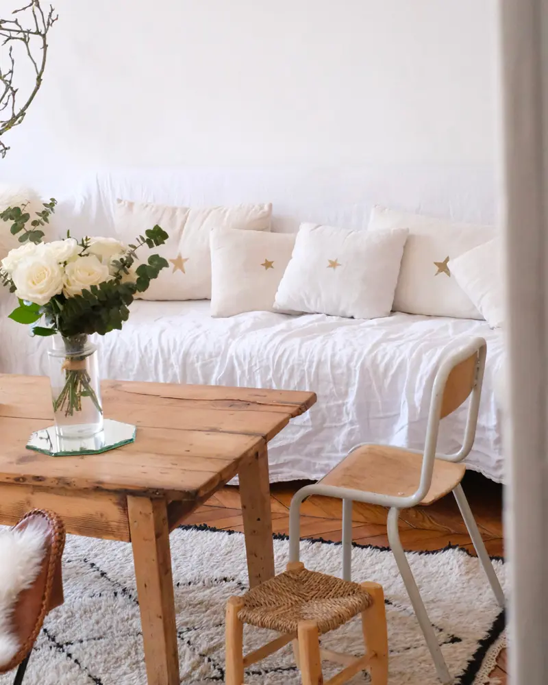 Rustic wood table with white flowers, white daybed with star pillows and Berber rug