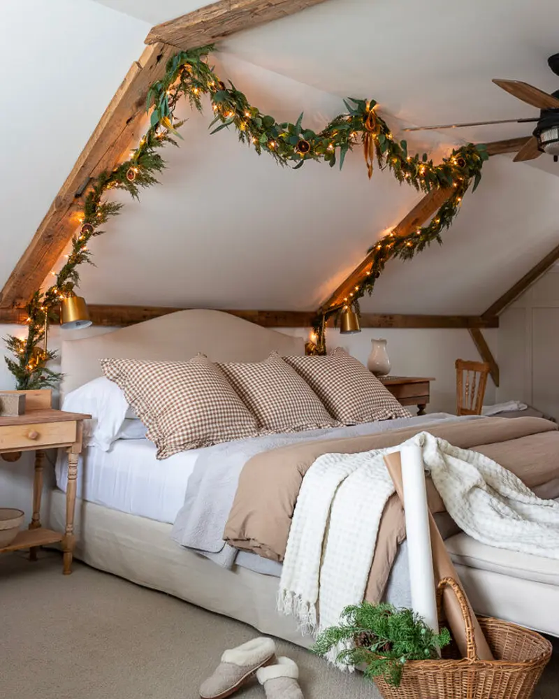 Lit garland along the beams of an attic bedroom with gingham pillows and a white knit throw