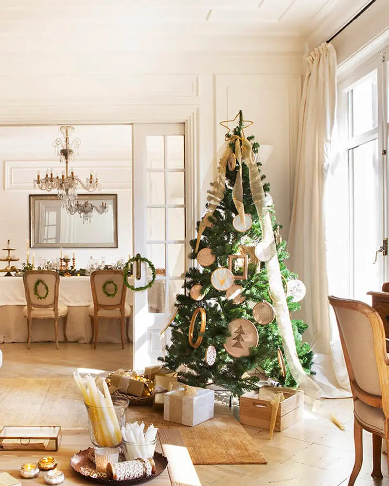 Tree with wood slice ornaments and cream ribbon in an elegant white room with a dining table and chandelier