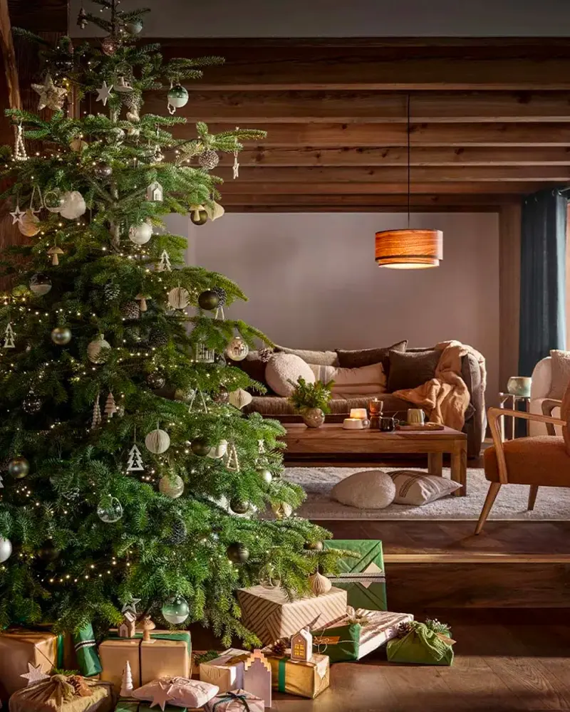 Large fir with wood and glass ornaments in front of a wood-paneled room with a glowing pendant