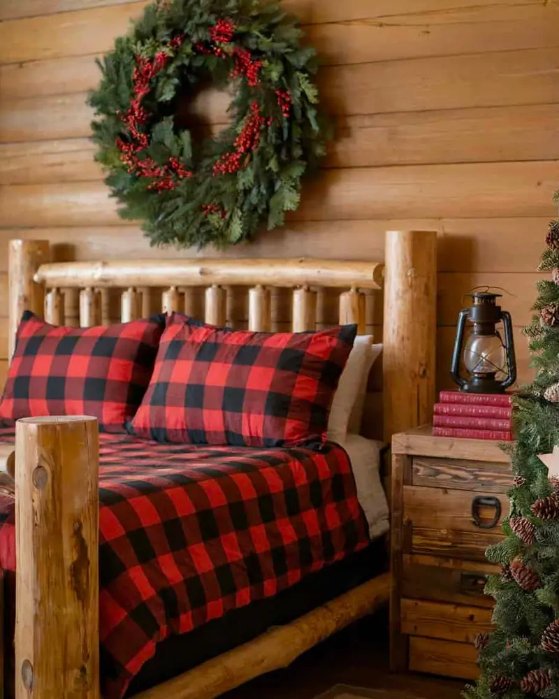 Log bed with red buffalo check bedding under a berry wreath on a log wall
