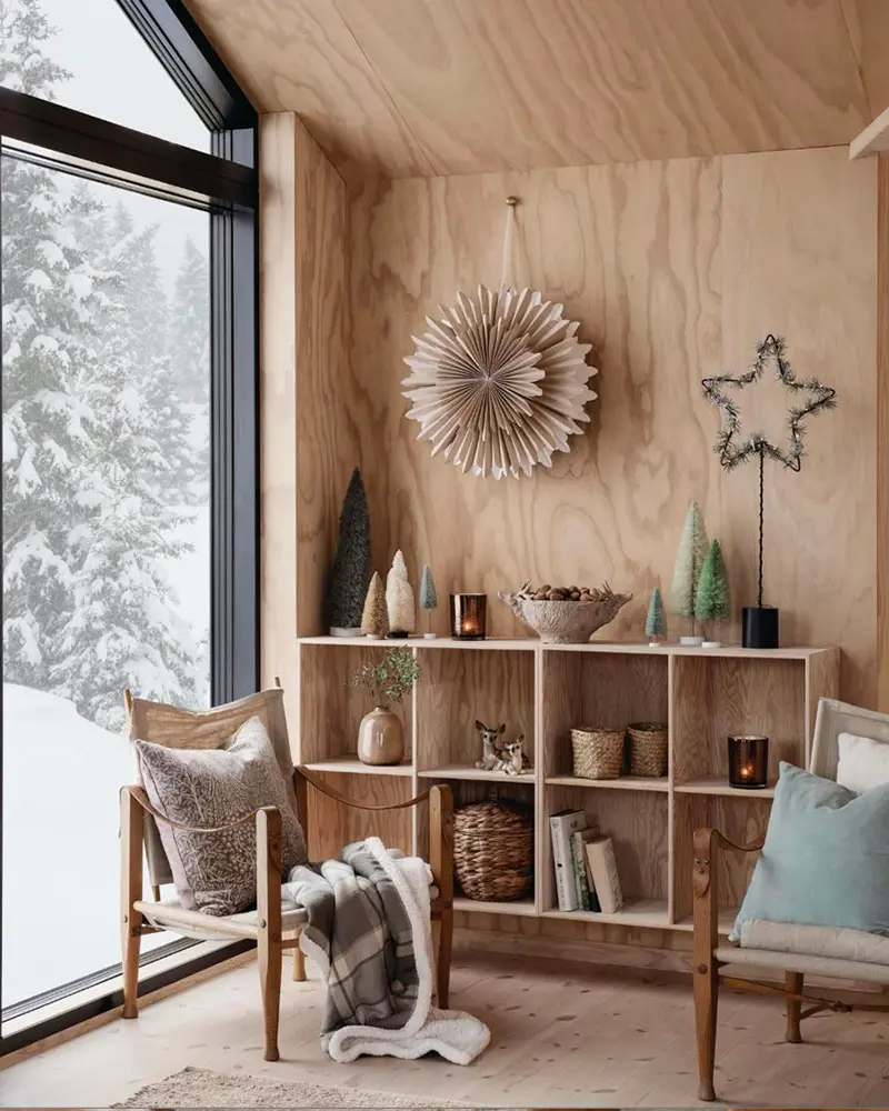 Plywood-lined nook with a paper star, a black wire star, cube shelving and a snowy view