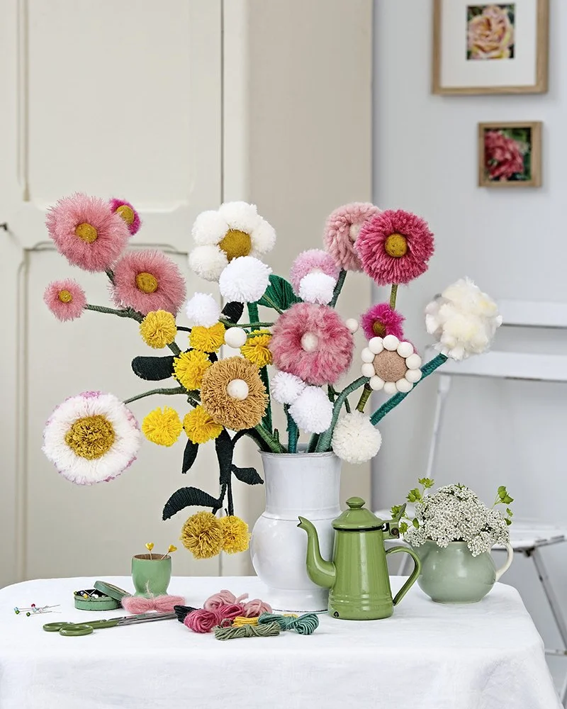 Bouquet of pink, white and yellow yarn pom-pom flowers in a white pitcher on a table
